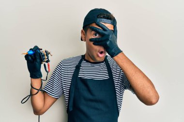 Genç, Afro-Amerikan erkek dövme sanatçısı profesyonel üniforma giyiyor ve eldiven taşıyor. Dövme makinesi elinde. Şok edici bir şekilde yüzünü ve gözlerini gizliyor.. 