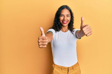 Afro-Amerikalı genç bir kız günlük giysiler giyip olumlu jestler yapıyor. Elleriyle gülümsüyor ve başarı için seviniyor. kazanan jest. 