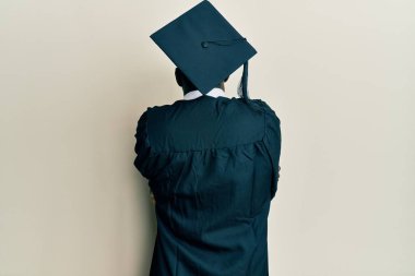 Mezuniyet şapkası ve tören cübbesi takan yakışıklı siyahi bir adam mutlu ve pozitif bir şekilde kendine sarılıyor. Sevgi ve özgüven. 