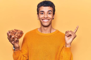 Genç Afrikalı Amerikalı adam elinde bademlerle kaseyle mutlu bir şekilde gülümsüyor. 