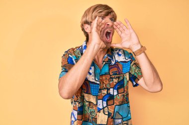 Yazlık tişört giyen genç sarışın adam elleri ağızda bağırarak bağırıyor. 