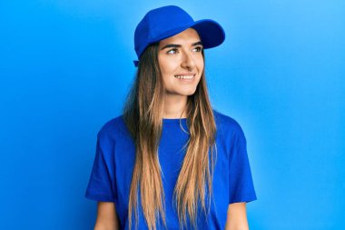 Teslimat üniforması giyen ve şapkalı genç İspanyol kadın yüzünde gülümsemeyle yan yana bakıyor, doğal bir ifade. Kendinden emin gülen. 