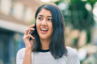 Genç İspanyol kadın gülümsüyor. Şehirdeki akıllı telefondan konuşuyor..