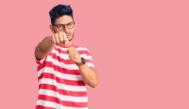 Yakışıklı Latin Amerikalı genç adam gündelik kıyafetler giyiyor ve gözlük takıyor dövüşmek için yumruk atıyor, agresif ve öfkeli saldırı, tehdit ve şiddet 