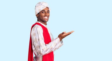 African handsome man wearing tradition sherwani saree clothes pointing aside with hands open palms showing copy space, presenting advertisement smiling excited happy 