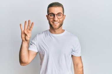 Kafkasyalı genç bir adam günlük kıyafetler ve gözlük takıyor. Dört numarayı gösteriyor ve işaret ediyor. Kendinden emin ve mutlu bir şekilde gülümsüyor.. 