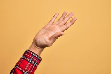 İzole edilmiş sarı arka plan üzerinde parmaklarını gösteren beyaz bir genç adam. Avuç içi açık bir şekilde destek ve yardım için uzanıyor.