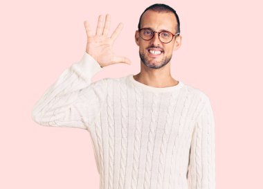 Genç, yakışıklı, günlük kıyafetler ve gözlük takan, beş numaralı parmaklarıyla işaret eden, kendinden emin ve mutlu bir şekilde gülümseyen adam.. 