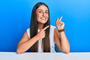 Masada oturmuş gülümseyen ve kameraya bakan, iki eliyle ve parmaklarıyla işaret eden İspanyol elbiseli güzel bir kadın.. 