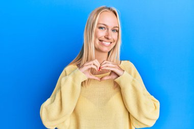 Sıradan kıyafetler giyen, aşık gülümseyen, elleriyle kalp sembolü yapan genç sarışın kız. romantik kavram. 