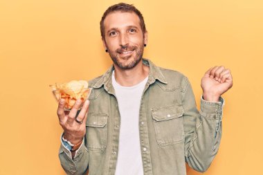 Patates cipsi tutan yakışıklı genç adam gururla bağırıyor, zaferi kutluyor ve başarıyı kollarını kaldırarak kutluyor. 