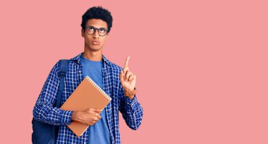 Afrika kökenli Amerikalı genç bir adam sırt çantasıyla elinde kitap tutarak üzgün ve üzgün görünüyor, parmaklarıyla yönü gösteriyor, mutsuz ve depresif.. 