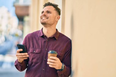 Genç İspanyol adam akıllı telefon kullanıyor ve şehirde kahve içiyor..