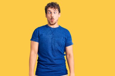 Kıvırcık saçlı, sıradan kıyafetler giyen, dudağında balık suratı olan, çılgın ve komik bir jest yapan genç yakışıklı bir adam. Komik ifade. 