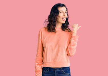 Genç ve güzel İspanyol bir kadın, günlük kıyafetler giyiyor, gülümsüyor, gülümsüyor ve başparmağıyla yan tarafa bakıyor.. 