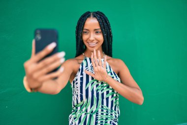 Genç Afrikalı Amerikalı kadın gülümseyerek şehirde akıllı telefon kullanarak video araması yapıyor..