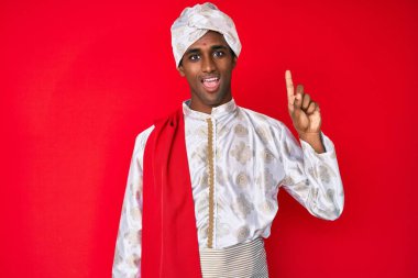 Yakışıklı Hintli adam geleneksel Sherwani sari giysisi giyiyor. Bir numarayı gösterip işaret ederken kendine güvenen ve mutlu gülümseyen.. 