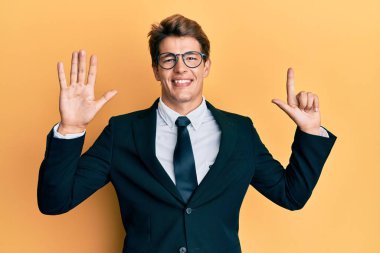 Yakışıklı, beyaz takım elbiseli ve kravatlı adam yedinci parmaklarını gösterip gösterirken kendinden emin ve mutlu gülümsüyor.. 