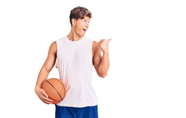 Genç yakışıklı adam basketbol topunu tutuyor başparmağıyla yan tarafa bakıyor mutlu bir şekilde ağzı açık gülümsüyor. 