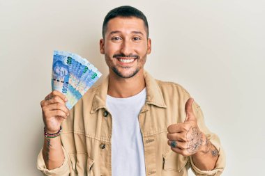 Dövmeleri olan yakışıklı bir adam Güney Afrika 'da 100 rand' lik banknotlar tutuyor mutlu ve olumlu gülümsüyor, başparmağı mükemmel ve onay işareti yapıyor. 
