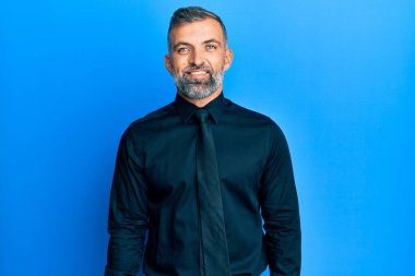 Orta yaşlı yakışıklı bir adam iş gömleği giyiyor ve yüzünde mutlu ve havalı bir gülümsemeyle kravat takıyor. şanslı kişi. 