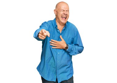 Orta yaşlı, kel bir adam sana gülüyor, eli vücudunun üzerinde kamerayı işaret ediyor, utanç ifadesi takınıyor. 