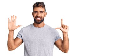 Gündelik kıyafetler giyen genç İspanyol adam yedi numarayı gösterip işaret ederken kendinden emin ve mutlu bir şekilde gülümsüyor.. 