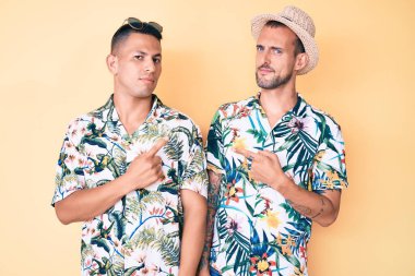 Yazlık şapkalı ve Hawaii tişörtlü iki genç gay, el parmaklarıyla reklamı gösteriyorlar, ciddi ve sakin bir yüz. 