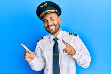 Sakallı yakışıklı bir adam, uçak pilotu üniforması giyiyor gülümsüyor ve kameraya bakıyor.. 