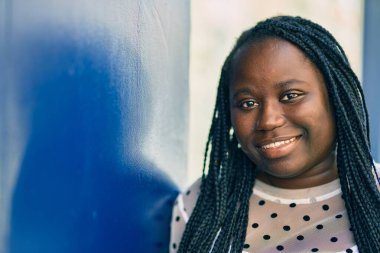 Genç Afrikalı Amerikalı kadın gülümseyerek şehirde mutlu mesut duruyor..