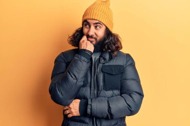 Gündelik kışlık giysiler giyen genç Arap adam ciddi bir yüz ifadesi, eli çeneli soru soran, kafa karıştırıcı bir fikir hakkında düşünceli. 