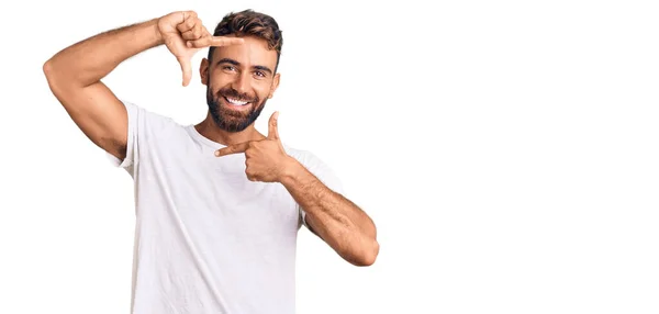 カジュアルな白いTシャツを着た若いヒスパニック系の男性は 幸せな顔で手や指でフレームを作り笑顔 創造性と写真の概念 — ストック写真