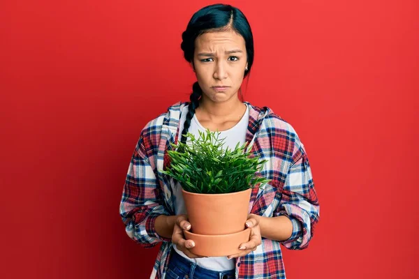 Beautiful Hispanic Woman Wearing Gardener Shirt Holding Plant Pot Skeptic — Stock Photo, Image