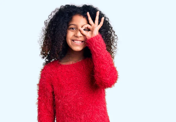 アフリカ系アメリカ人の子供とともに巻き毛を身に着けていますカジュアル冬のセーター笑顔幸せな行いますOkサインとともに手で目を通して見る — ストック写真