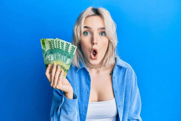 Young Blonde Girl Holding Indonesian Rupiah Banknotes Scared Amazed Open — Stock Photo, Image