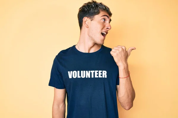 Young Handsome Man Wearing Volunteer Shirt Pointing Thumb Side Smiling — Stok fotoğraf