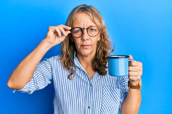 中年金发碧眼的女人戴着眼镜 喝着一杯疑神疑鬼和紧张的咖啡 皱着眉头因为问题而心烦意乱 消极的人 — 图库照片