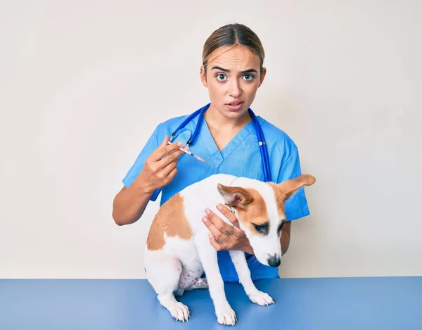 若い美しいブロンドの獣医師の女性は 犬の懐疑的で神経を子犬にワクチンを入れて 問題のために動揺を眉をひそめています 否定的な人 — ストック写真