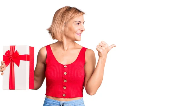 Ung Blond Kvinna Håller Gåva Pekar Tummen Upp Till Sidan — Stockfoto