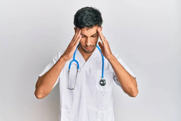 年轻英俊的男人穿着医生制服 头戴听诊器 因为压力头疼 偏头痛 — 图库照片