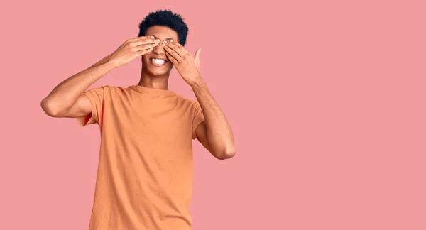 笑顔で陽気で面白い手で目を覆うカジュアルな服を着ている若いアフリカ系アメリカ人男性 視覚障害の概念 — ストック写真