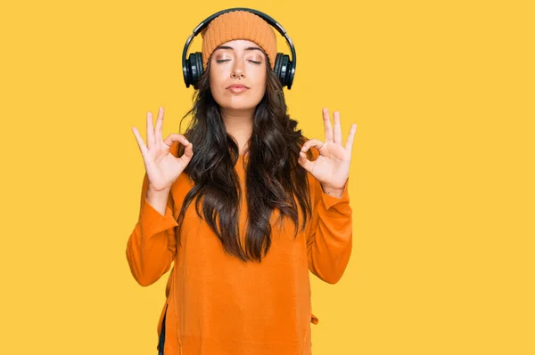 ヘッドフォンを使用して音楽を聴く美しいブルネットの若い女性は 指で瞑想のジェスチャーをして閉じ目でリラックスして笑顔 ヨガのコンセプト — ストック写真