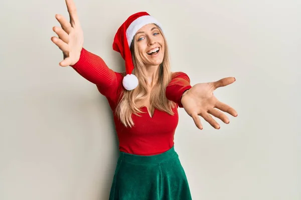 美丽的高加索女人 身穿圣诞服装 头戴一顶帽子 看着镜头 张开双臂拥抱 欢快的表达拥抱幸福 — 图库照片