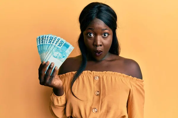 African Young Woman Wearing Doctor Uniform Holding 100 Brazilian Reals — Stock Photo, Image