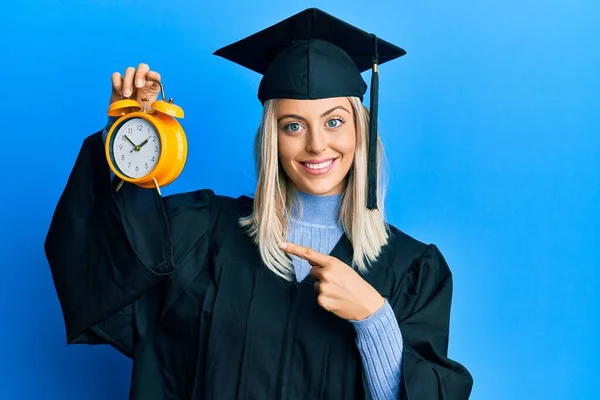 Piękna Blondynka Nosi Czapkę Szlafrok Ceremonii Trzymając Budzik Uśmiechając Szczęśliwy — Zdjęcie stockowe