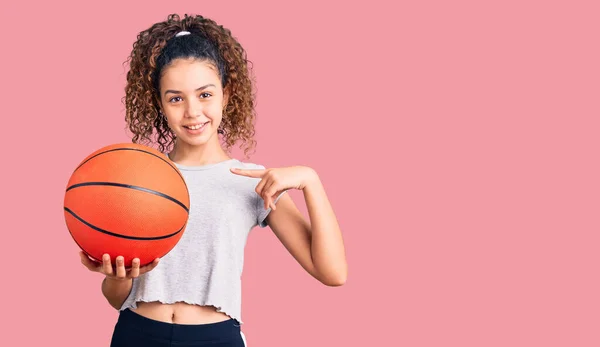 Hermosa Niña Con Pelo Rizado Sosteniendo Pelota Baloncesto Señalando Dedo —  Fotos de Stock