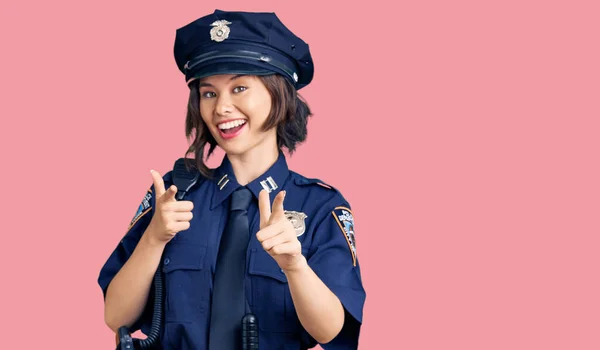 Young beautiful girl wearing police uniform pointing fingers to camera with happy and funny face. good energy and vibes.