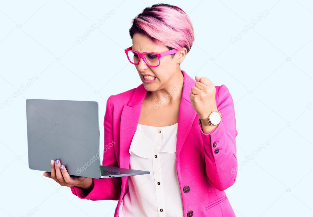 Young beautiful woman with pink hair wearing glasses holding laptop annoyed and frustrated shouting with anger, yelling crazy with anger and hand raised 