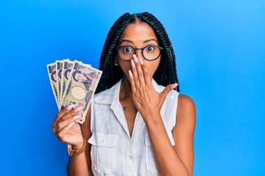 Japon yen banknotları tutan güzel İspanyol kadın ağızlarını eliyle kapatıyor, şaşırmış ve hata yapmaktan korkuyor. şaşırmış ifade 