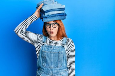 Güzel kızıl saçlı kadın, katlanmış kot pantolonları kafasının üstünde tutuyor. Şaşırmak için ağzı açık ve korkmuş, inançsız bir yüz. 